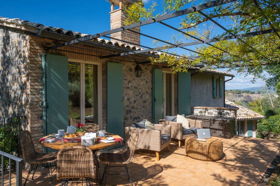 The stone loggia with its pergola, wicker chairs and a laid breakfast table